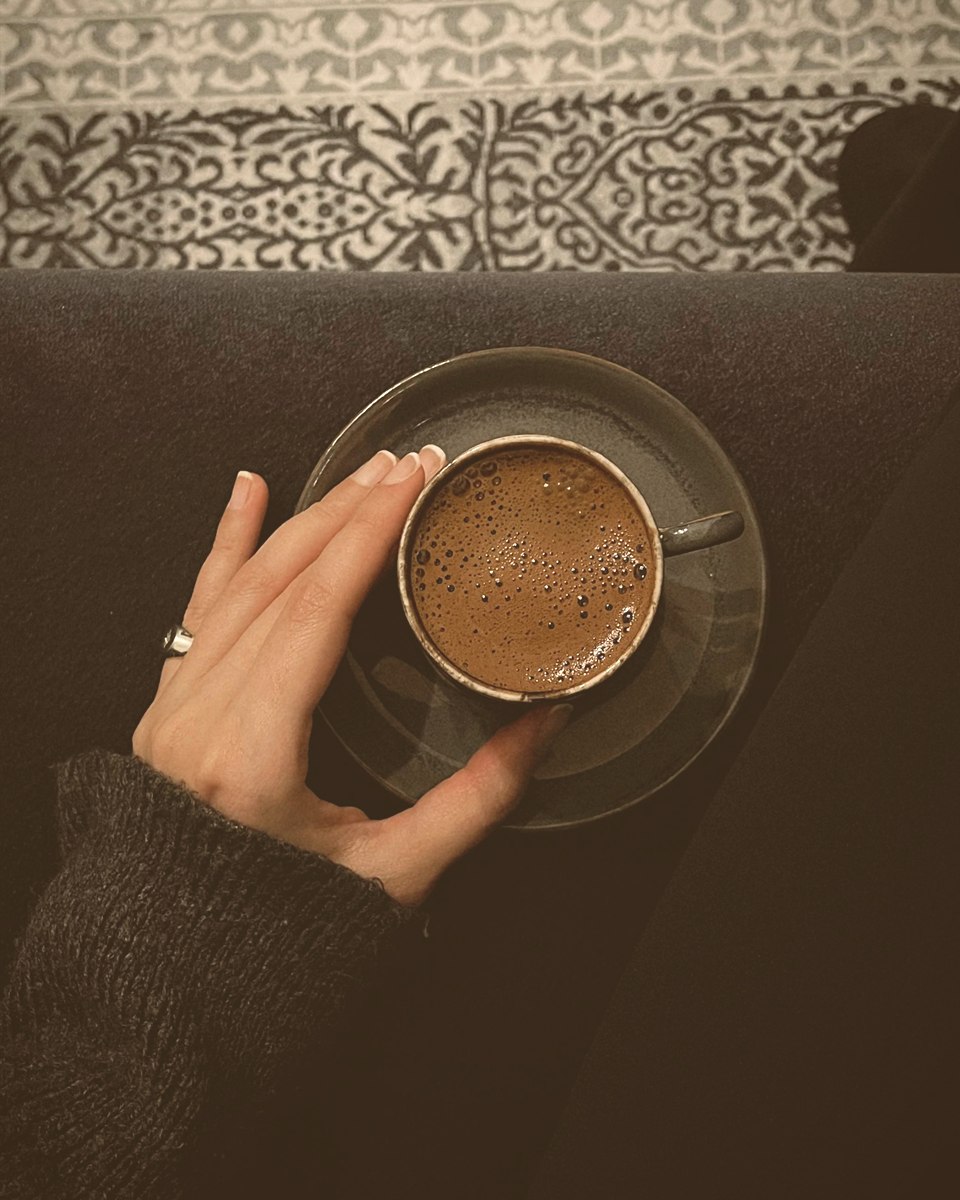 Eine Hand ruht an einer Tasse Kaffee auf einer dunklen Decke