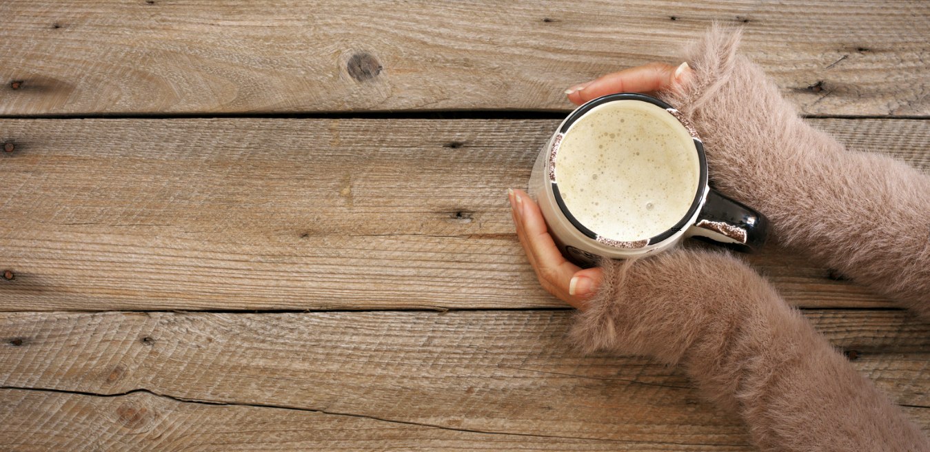 Zwei Hände halten eine Tasse Kaffee auf einem Holztisch