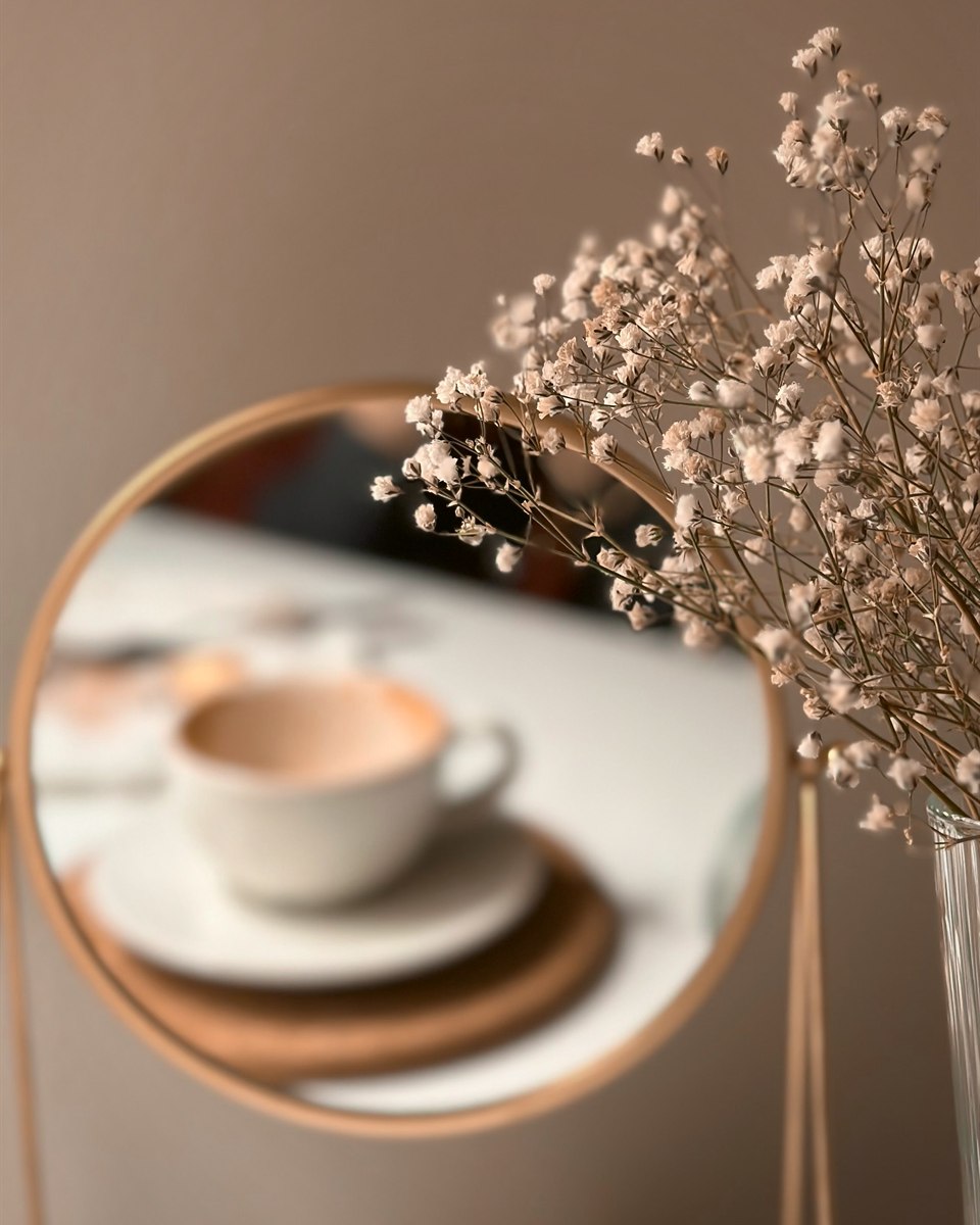 Trockenblumen vor einem runden Spiegel, darin eine Kaffeetasse